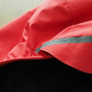 Kapuce s pruženkou, reflexním proužkem a měkkým štítkem. Není na ni stahování, ale to nijak nevadí. Pod kapuci se vleze i přilba.