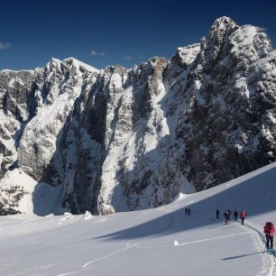 Traverz směrem ke Kotovu sedlu se skalnatým hřebenem Šite v pozadí. Skialpinistická túra nad Kotovo sedlo pod severními srázy Jalovce v Julských Alpách.