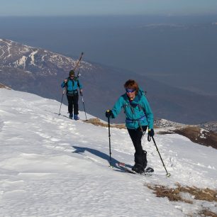 Splitboardistka šlape na tuleních pásech, zatímco skialpinista nese lyže na zádech - makedonské pohoří Šar planina