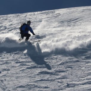 Ve strmém terénu předbíhá sníh z předchozího oblouku lyžaře