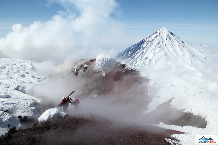 Roman a Matúš prochází fumaroly na vrcholu vulkánu Avačinskaja, v pozadí vulkán Korjakskij