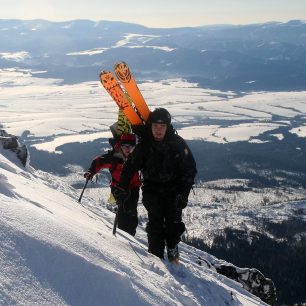 Široké lyže připevněné v čele batohu vedle sebe - obdobné připevnění snowboardu